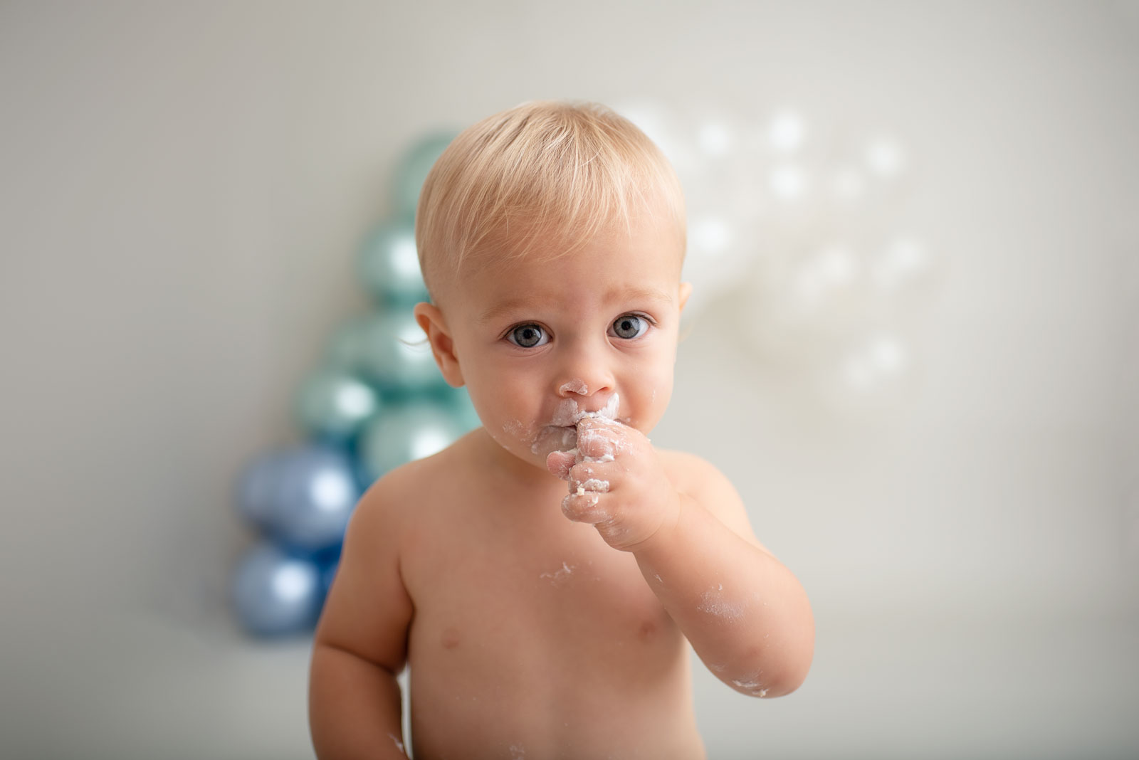 little boy eating cake with a balloon arch behind him