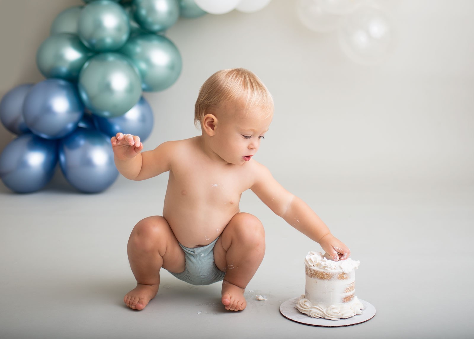 little boy squatting with his hand in cake