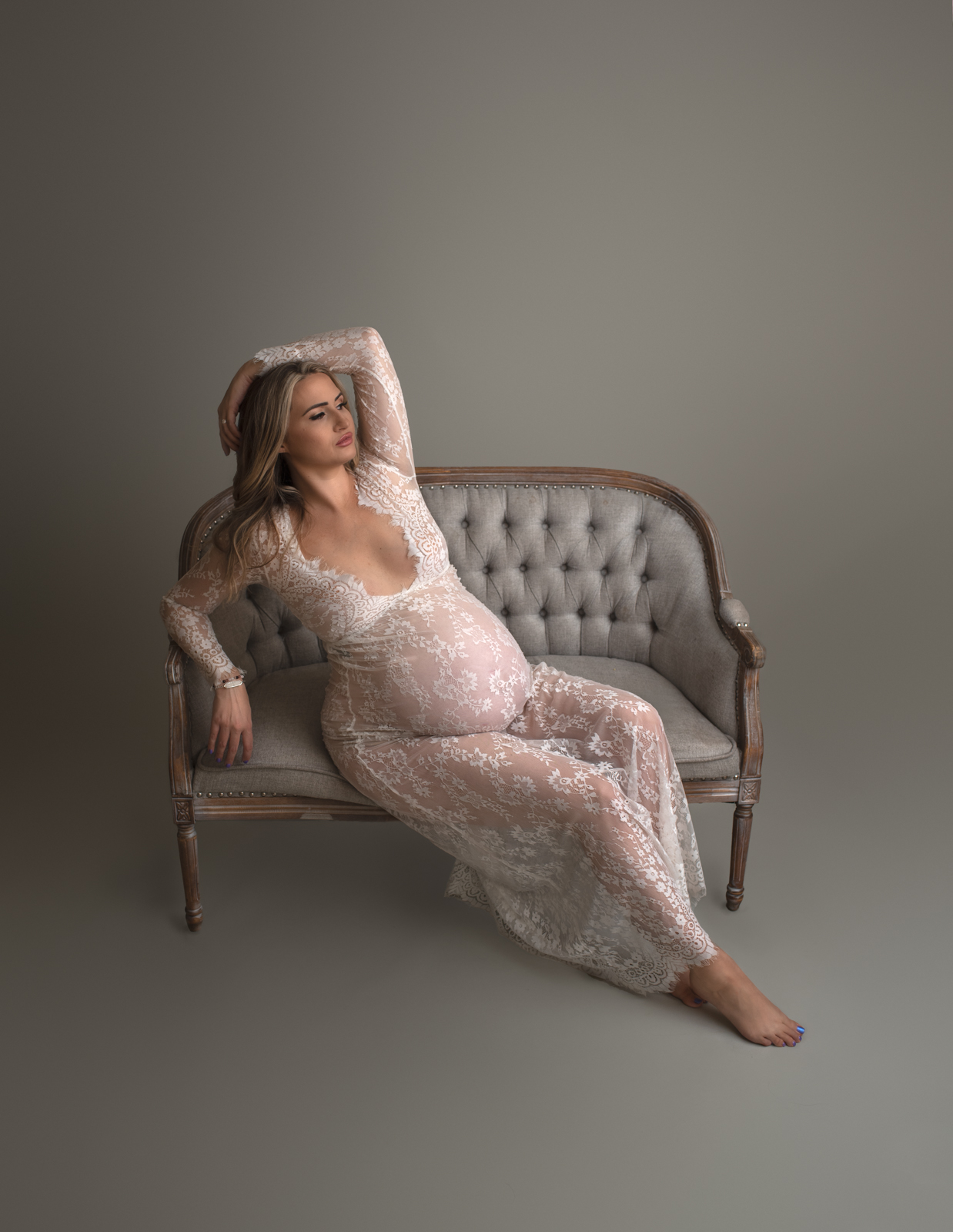 mom to be in sheer white maternity gown laying on a grey loveseat St. Louis Prenatal Yoga