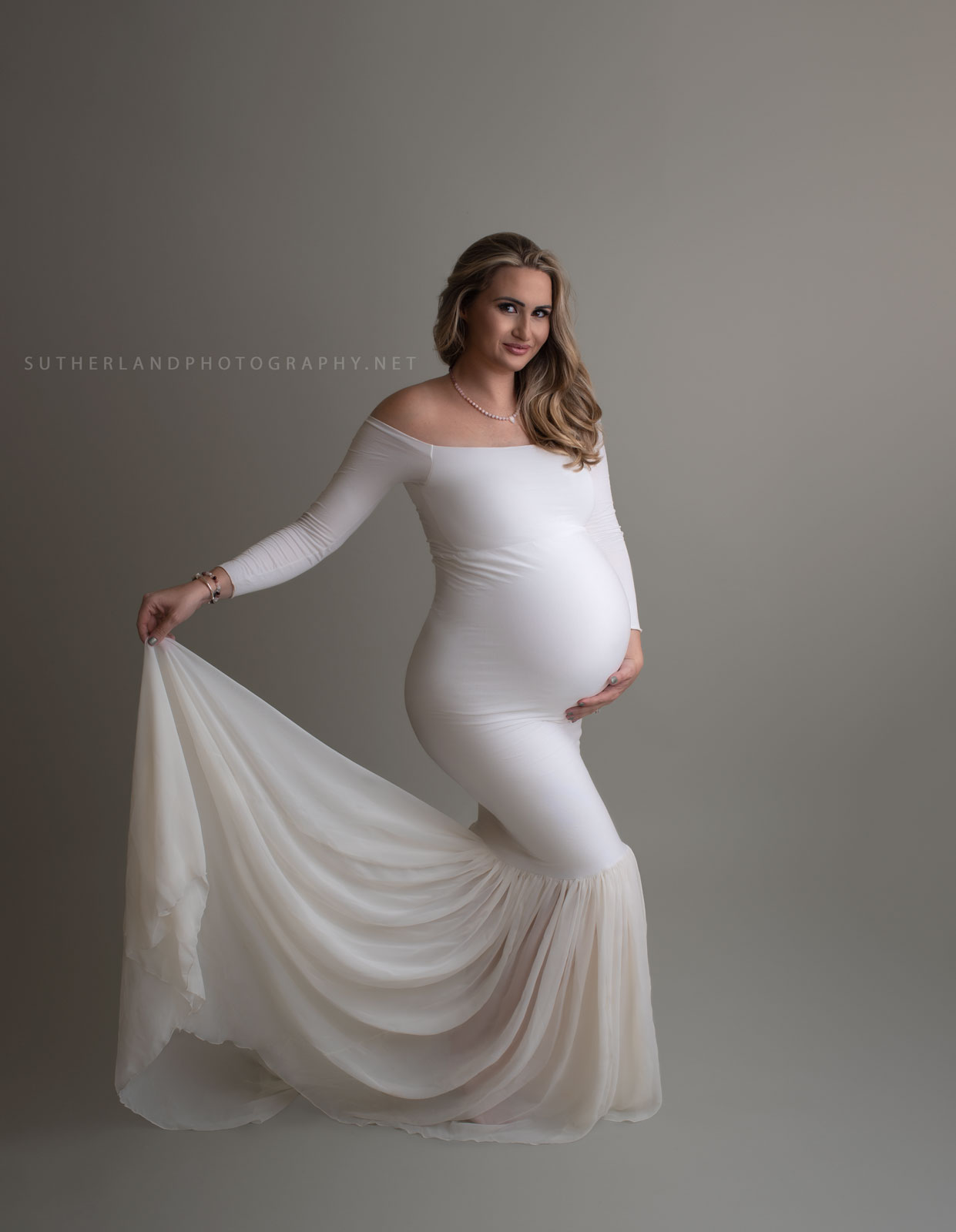 Mother to be stands in a studio wearing a white materrnity gown dancing for birth