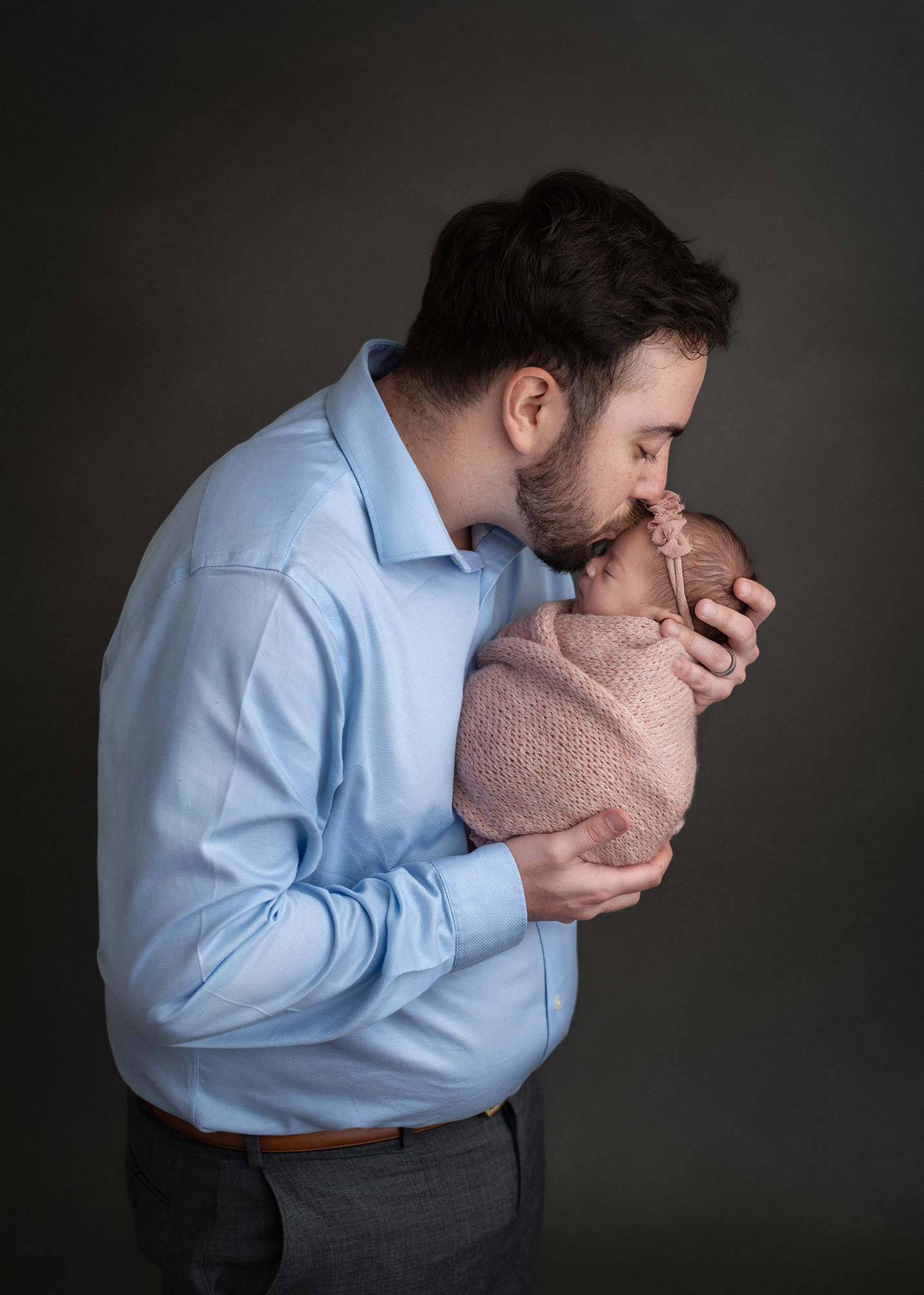 new dad in a blue shirt kissing his new daughter on the head