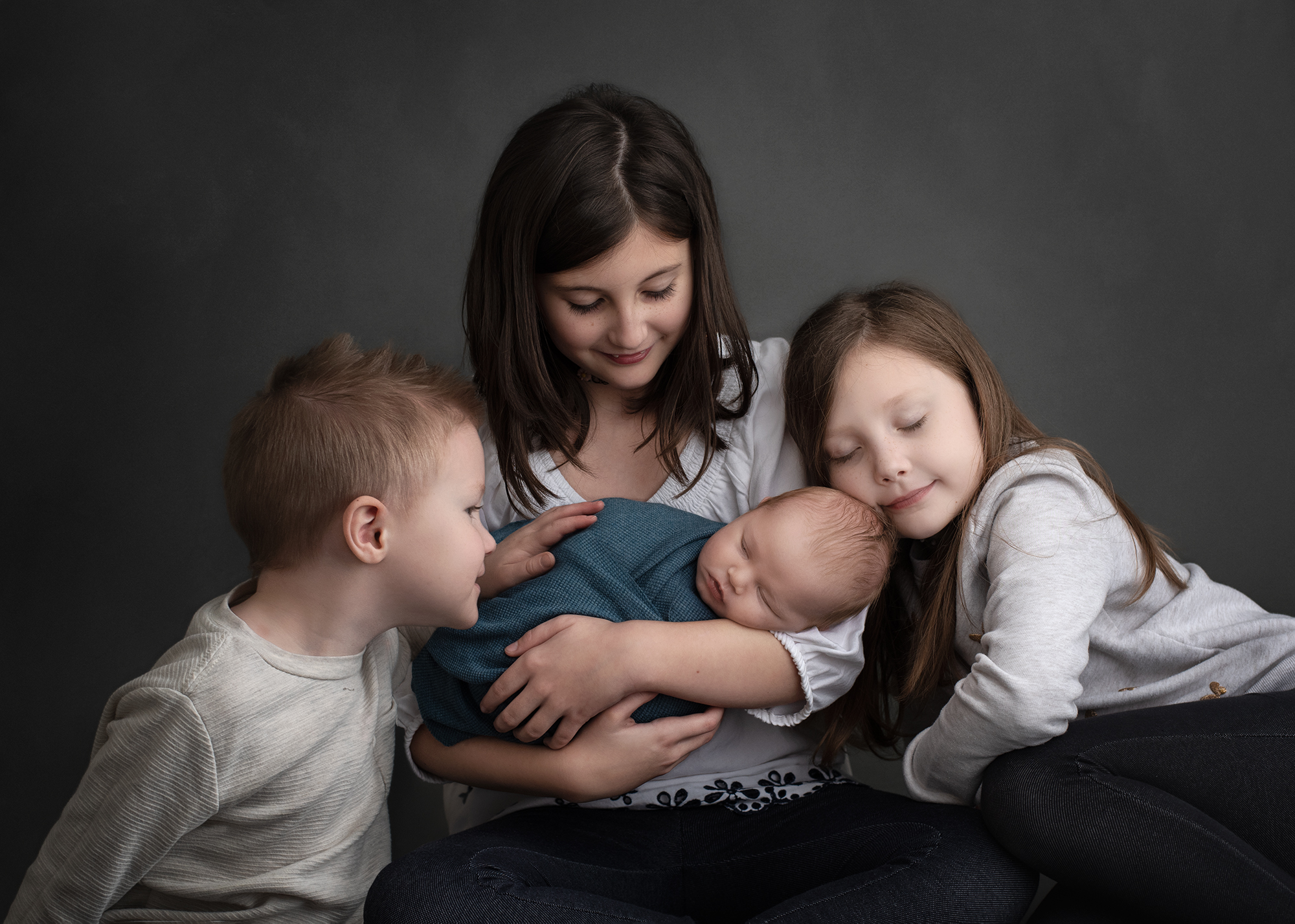 A newborn baby sleeps in the arms of older sister while another sister leans on her shoulder and young brother leans in honeycomb st louis