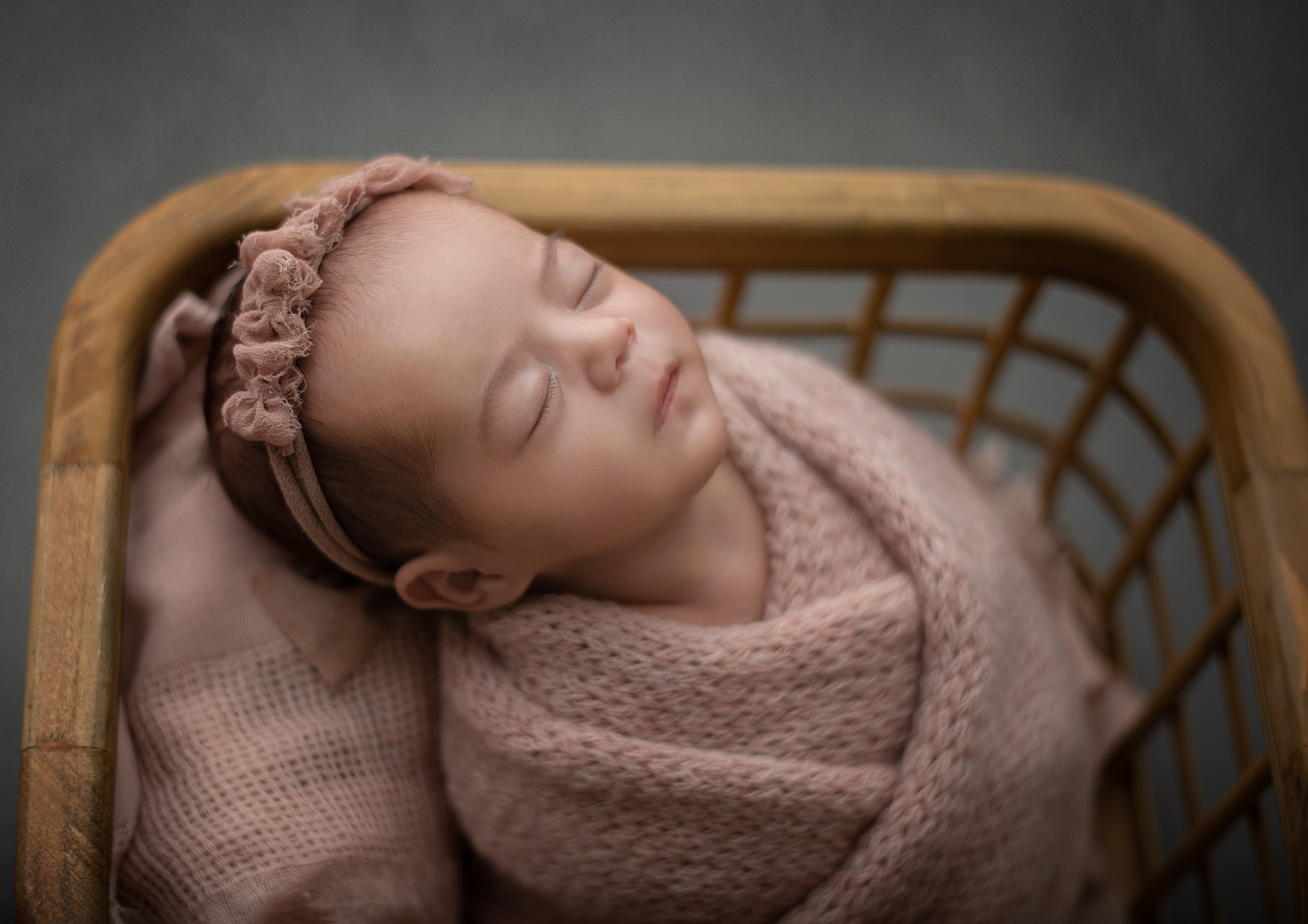 A newborn baby sleeps in a knit swaddle in a wooden basket kangaroo kids st louis