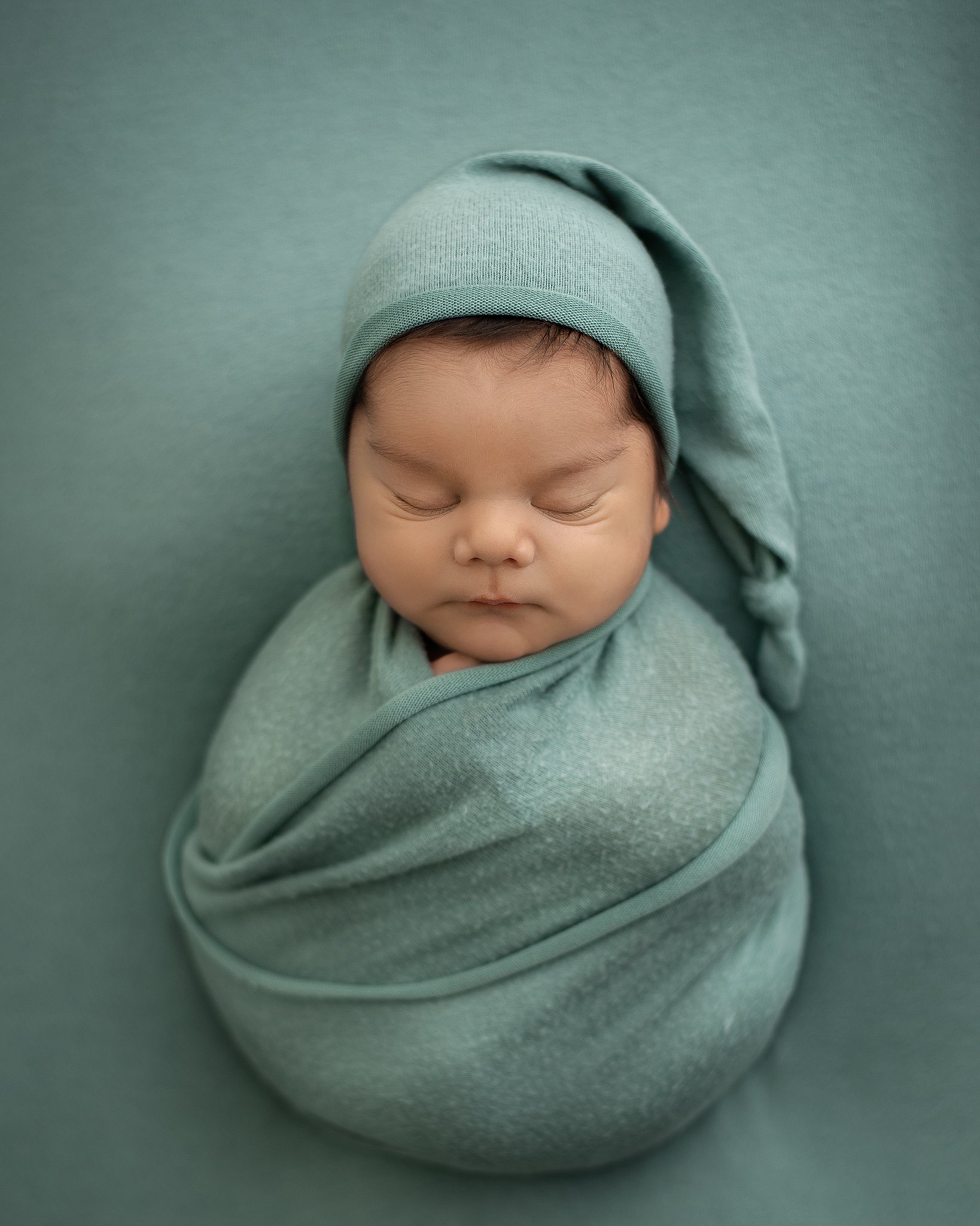 A newborn baby sleeps in a ball swaddle with a matching nightcap town and country pediatricians
