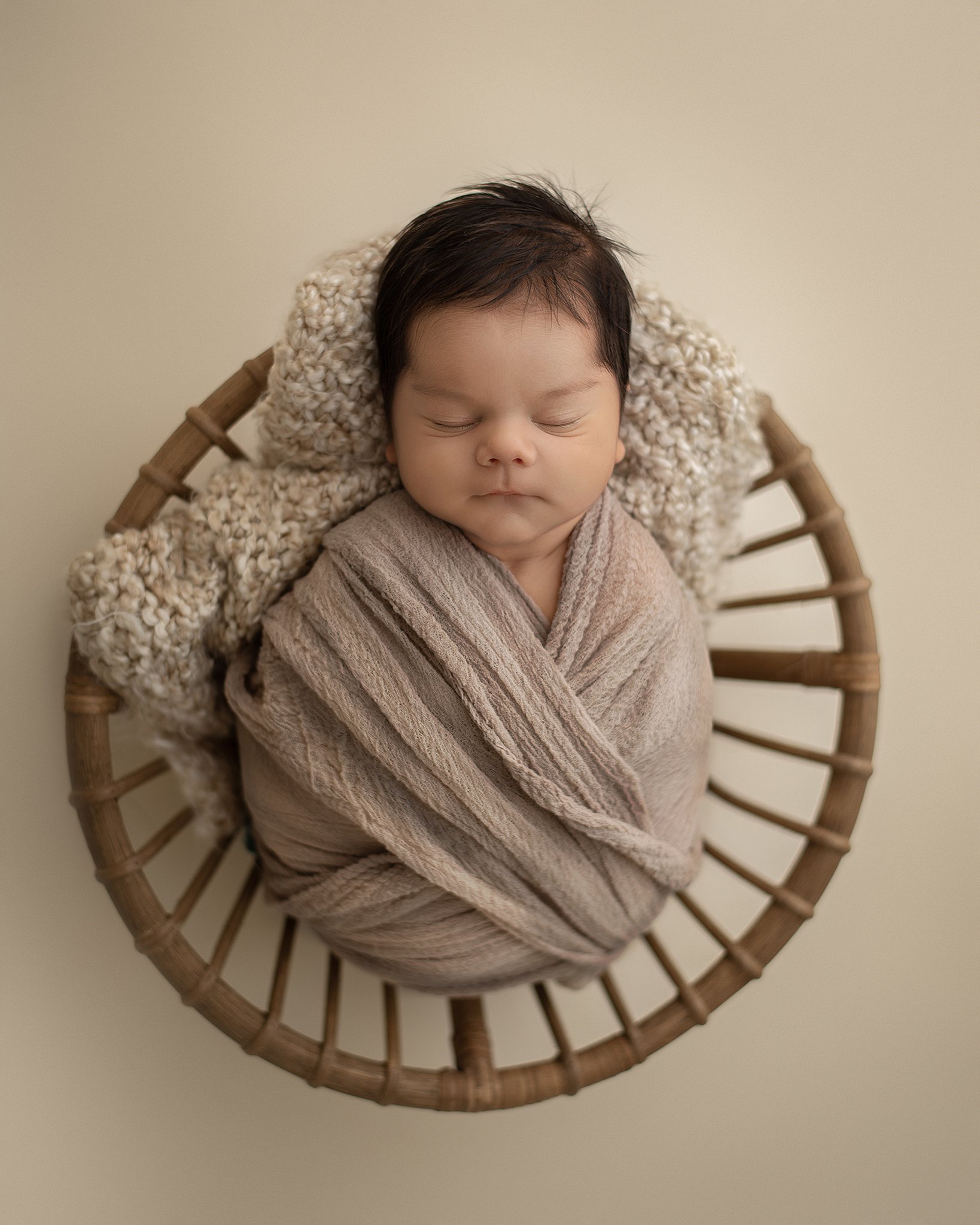 A newborn baby sleeps in a brown swaddle in a wicker basket town and country pediatricians