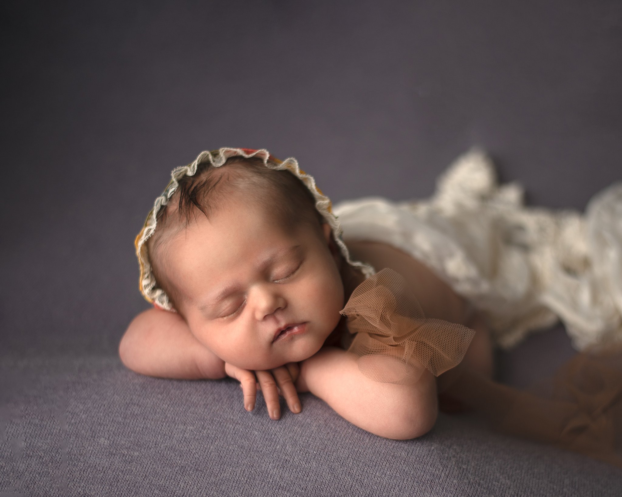A newborn baby sleeps on folded hands in a bonnet lake st louis pediatricians