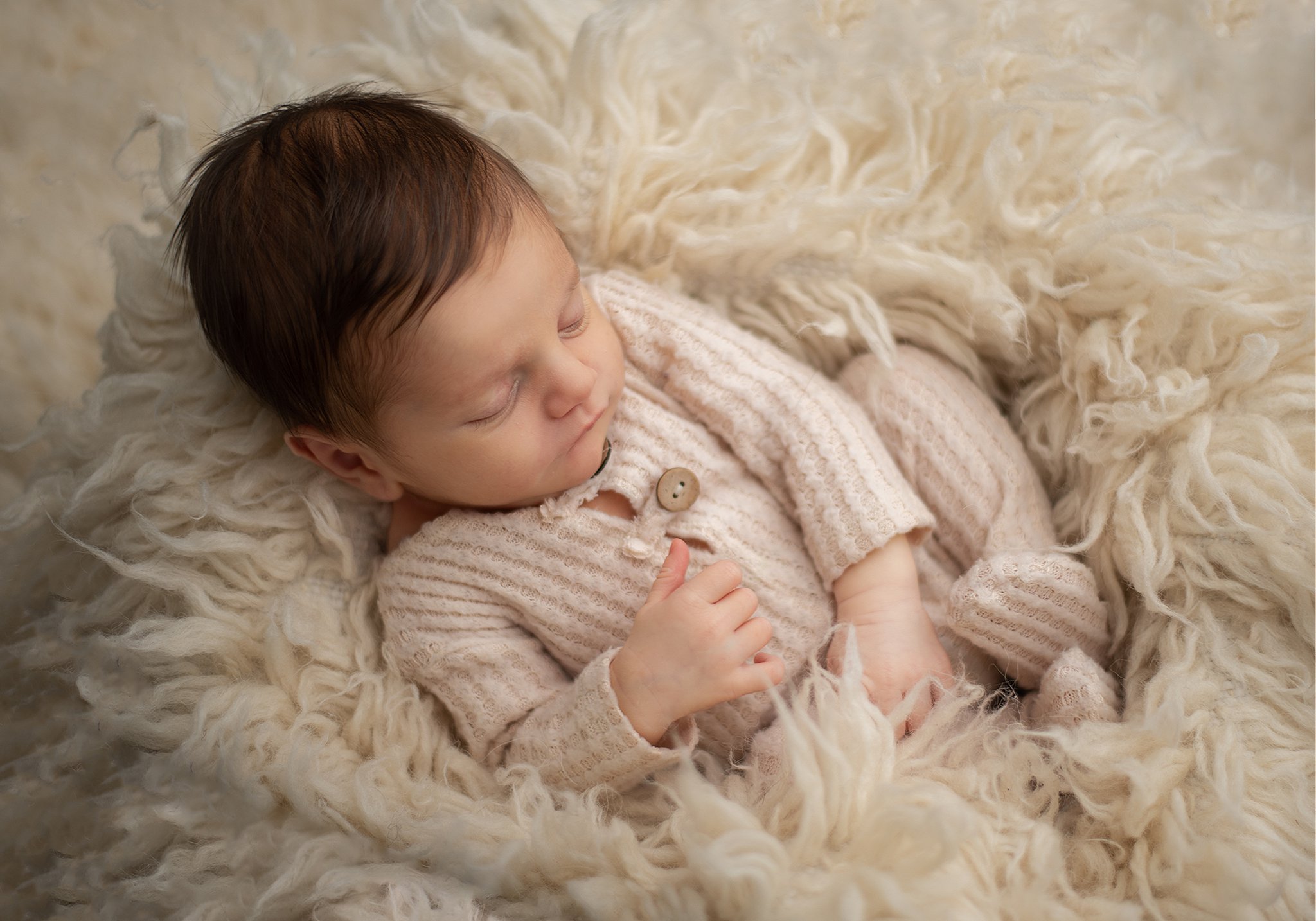 A newborn baby sleeps in a bed of fur in a knit onesie
